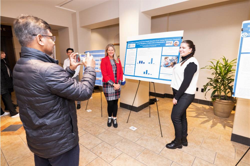 Faculty member Dr. Azizur Molla (far left) taking a photo of participant Isabella (far right) and Graduate Program Director Dr. Ranelle Brew (middle). 
